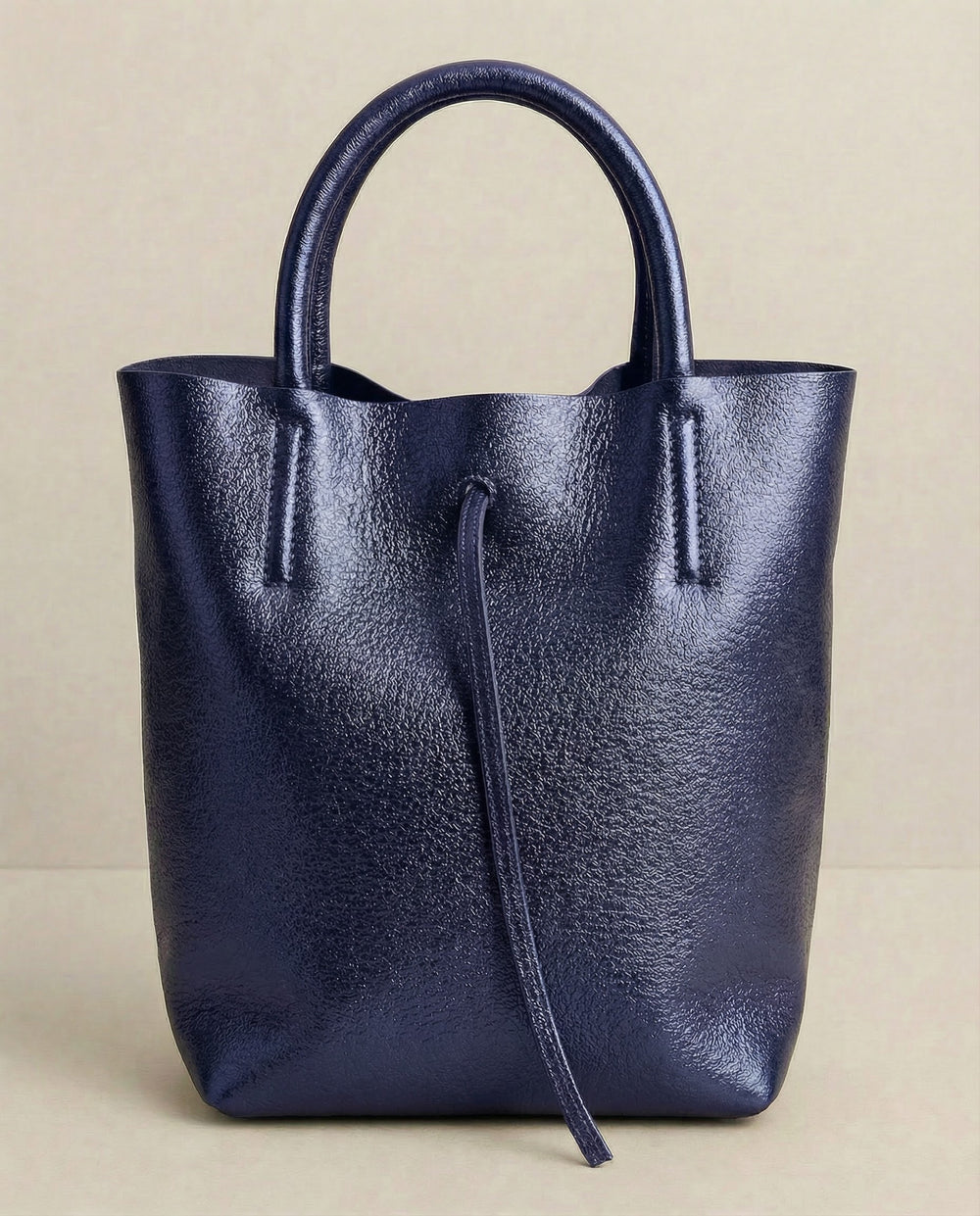 Mini tote in metallic indigo leather with structured silhouette and top handles, sleek and compact design.