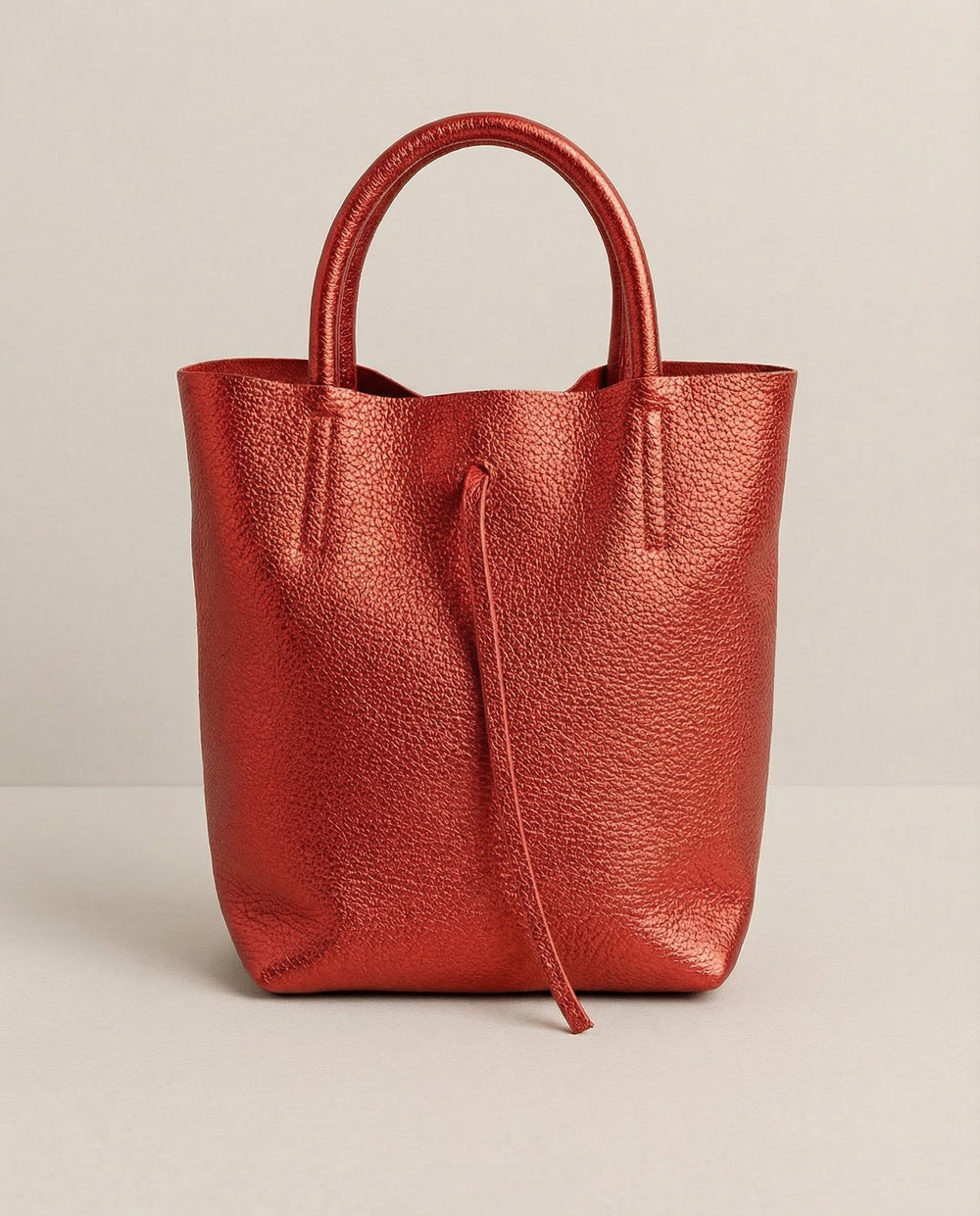 Mini tote in metallic red leather with structured silhouette and top handles, sleek and compact design.