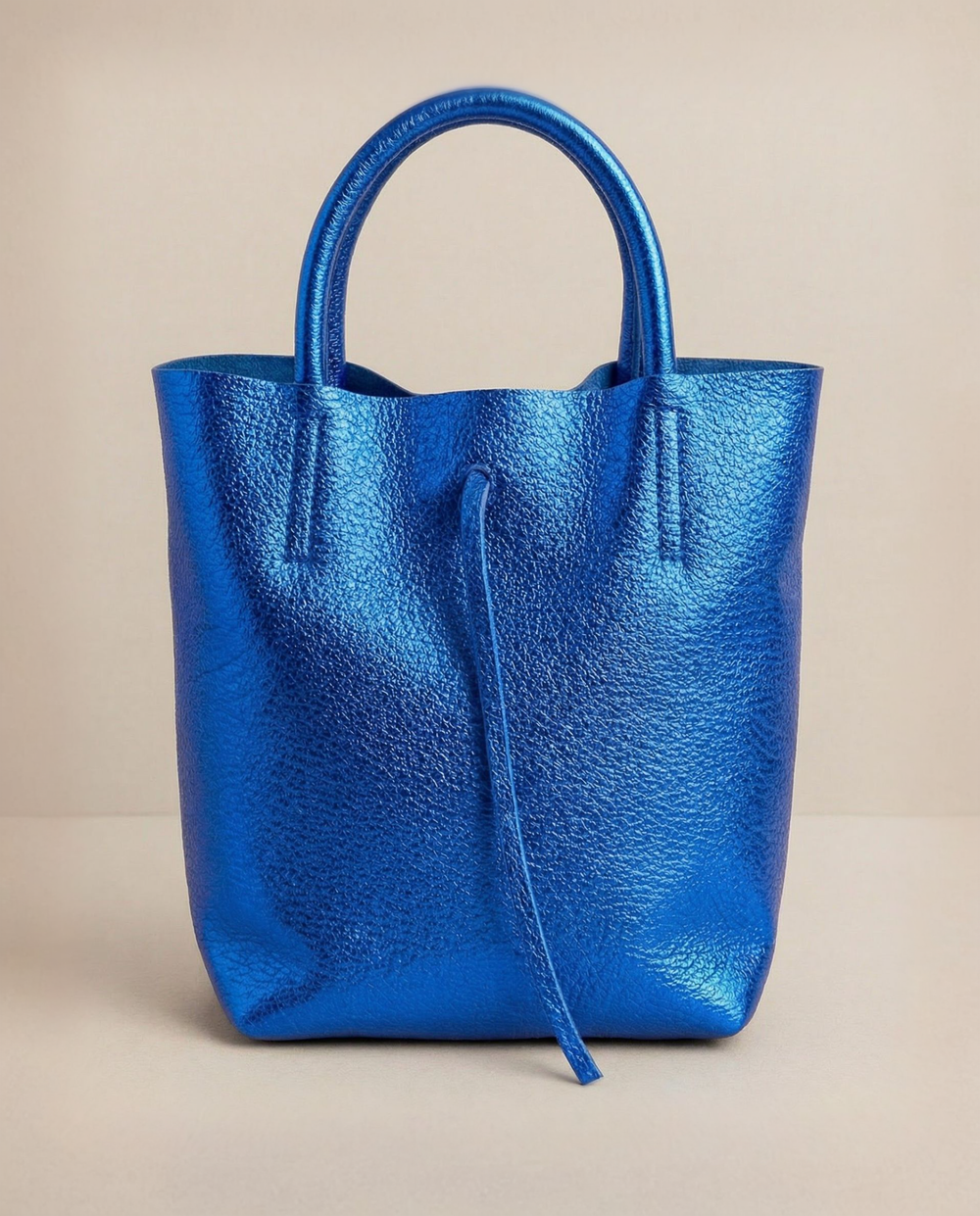 Mini tote in metallic royal blue leather with structured silhouette and top handles, sleek and compact design.