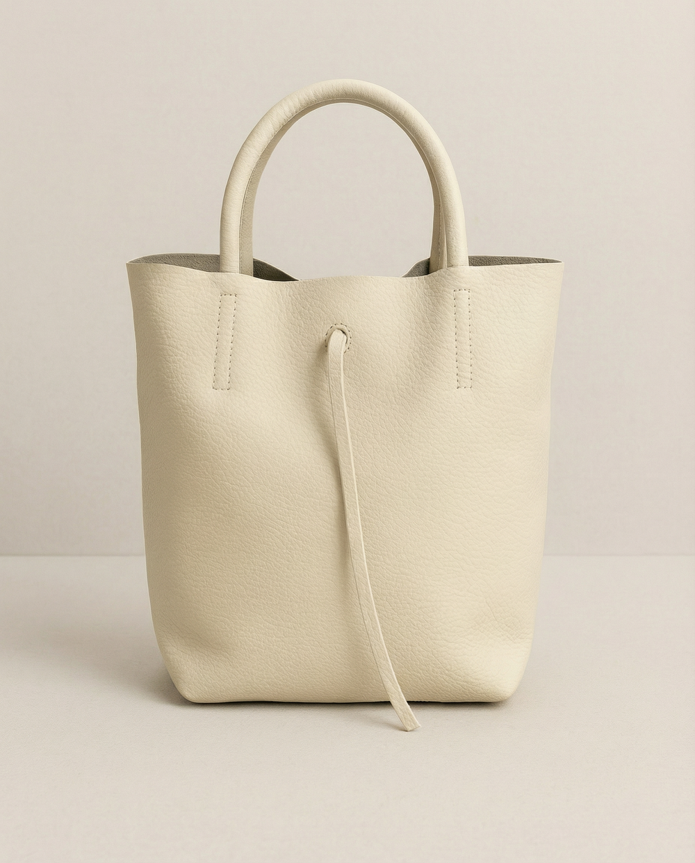 Ivory pebble leather mini tote with structured silhouette, detachable crossbody strap, compact interior, and genuine Italian craftsmanship.