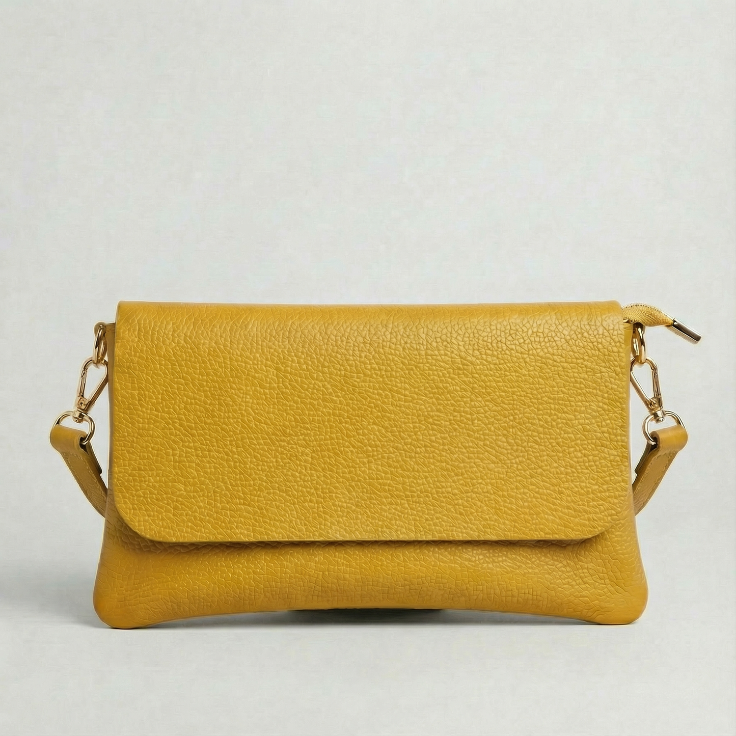 Mustard pebble leather crossbody bag with a matching color adjustable strap, displayed on a light gray background.