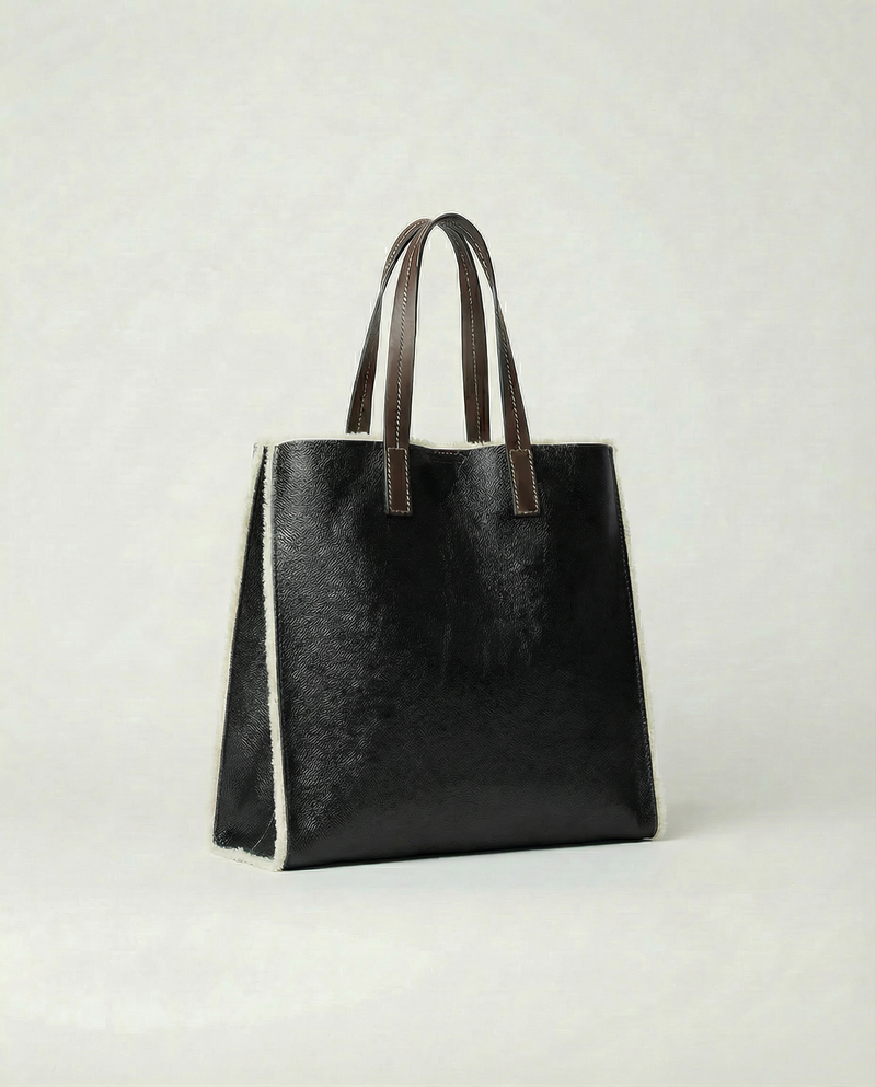 Black leather tote bag with brown handles on a light gray background