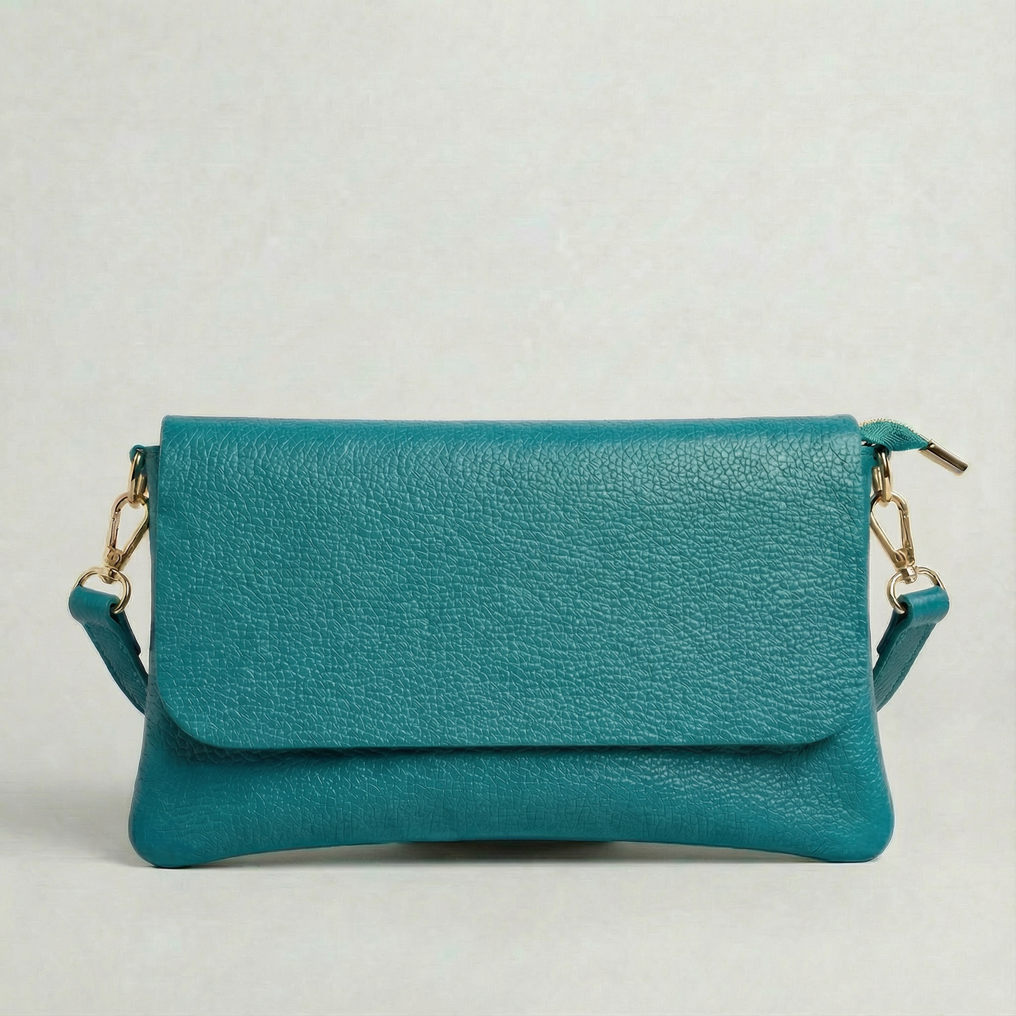Turquoise pebble leather crossbody bag with a matching color adjustable strap, displayed on a light gray background.