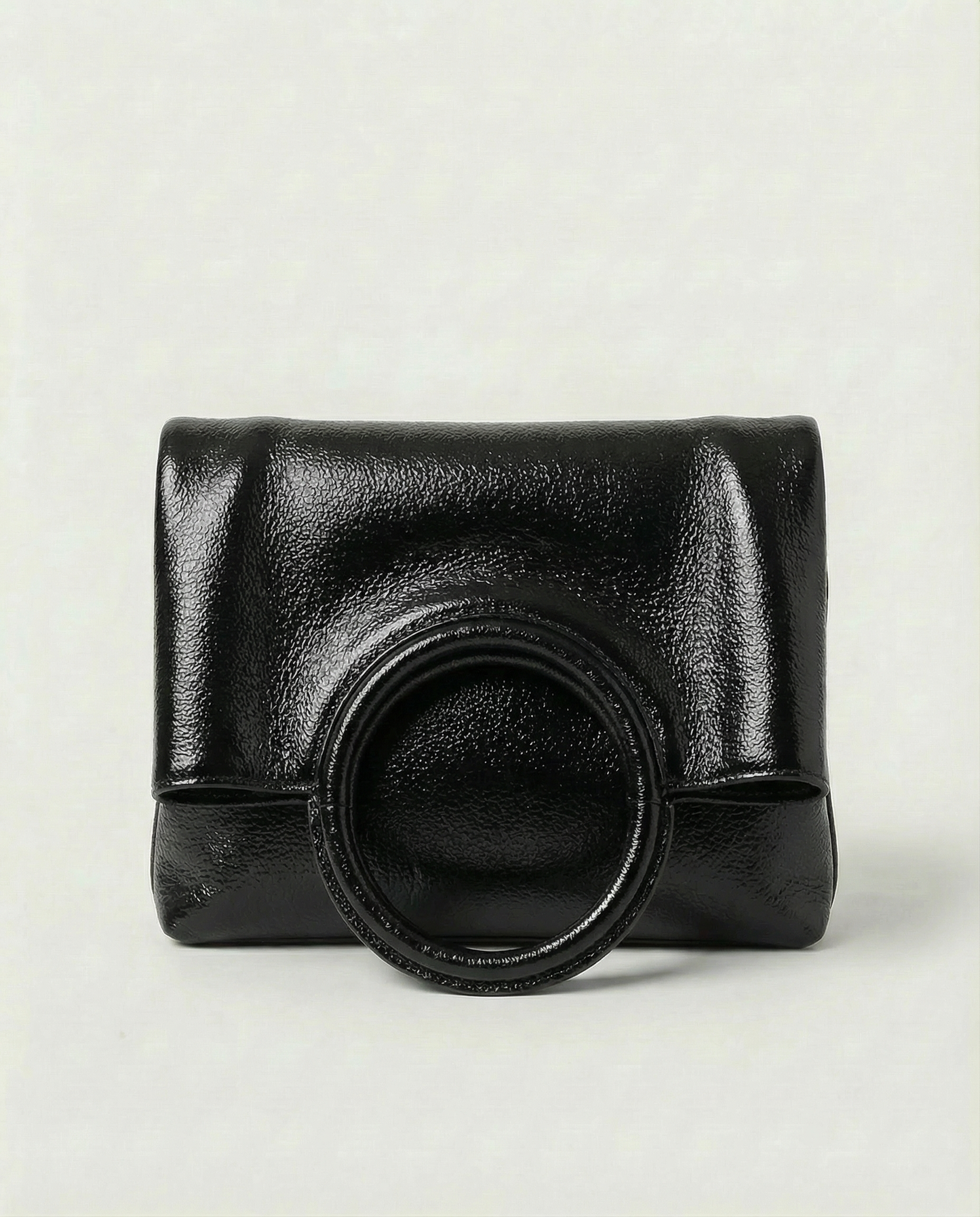 Metallic black leather ring bag with circular top handle and structured silhouette, sleek and modern design.
