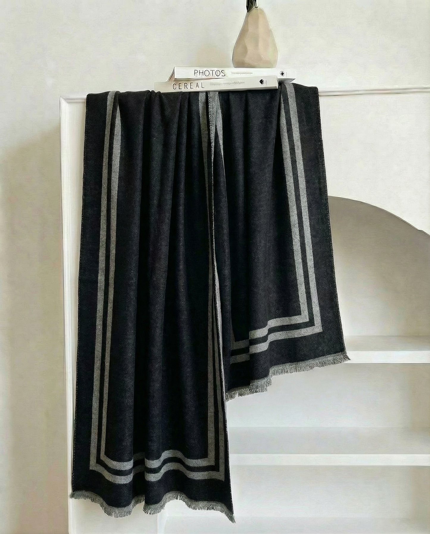Black scarf with gray stripes draped over a bookshelf against a neutral background