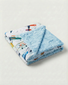 Folded blue blanket with cartoon plane design on a light gray background, view 1