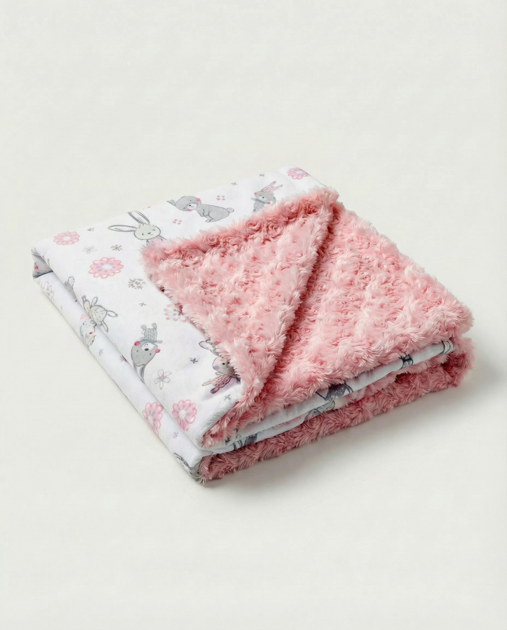 Folded pink blanket with floral and animal pattern on a light background