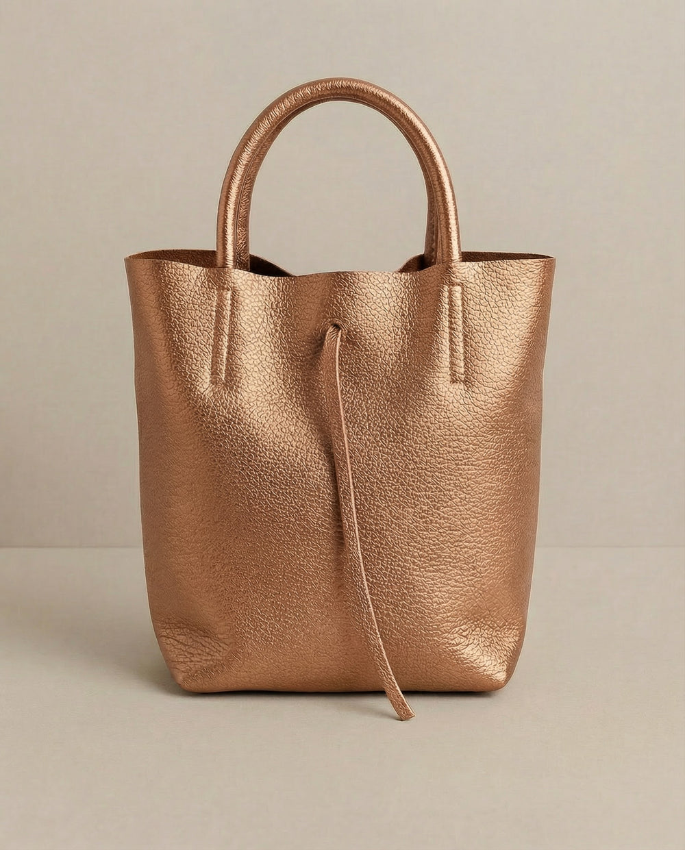 Mini tote in metallic copper leather with structured silhouette and top handles, sleek and compact design. 