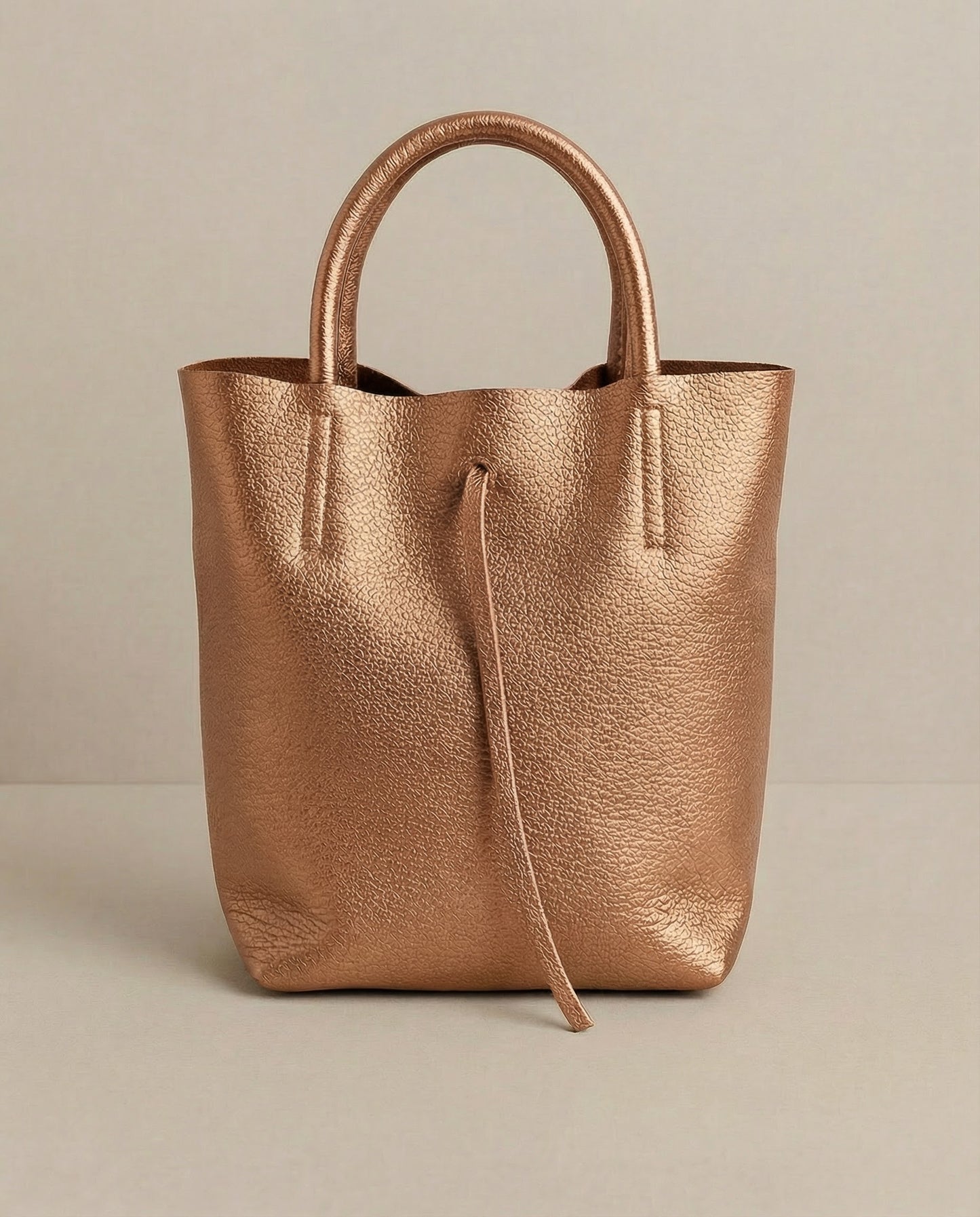 Mini tote in metallic copper leather with structured silhouette and top handles, sleek and compact design. 