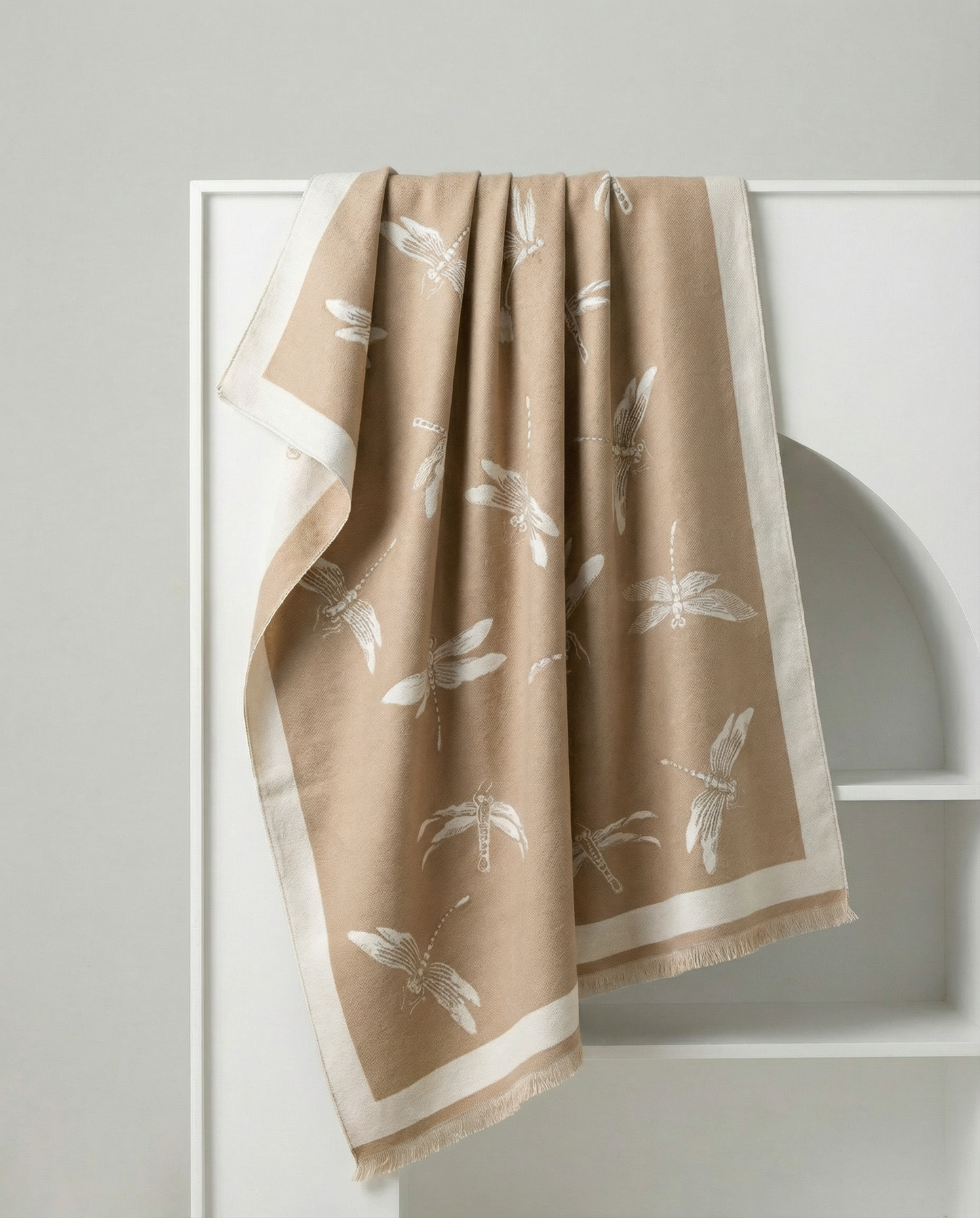 Beige wrap with white dragonfly patterns hanging on a white rack against a light gray wall.