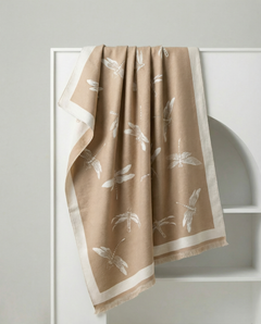 Beige wrap with white dragonfly patterns hanging on a white rack against a light gray wall., view 2