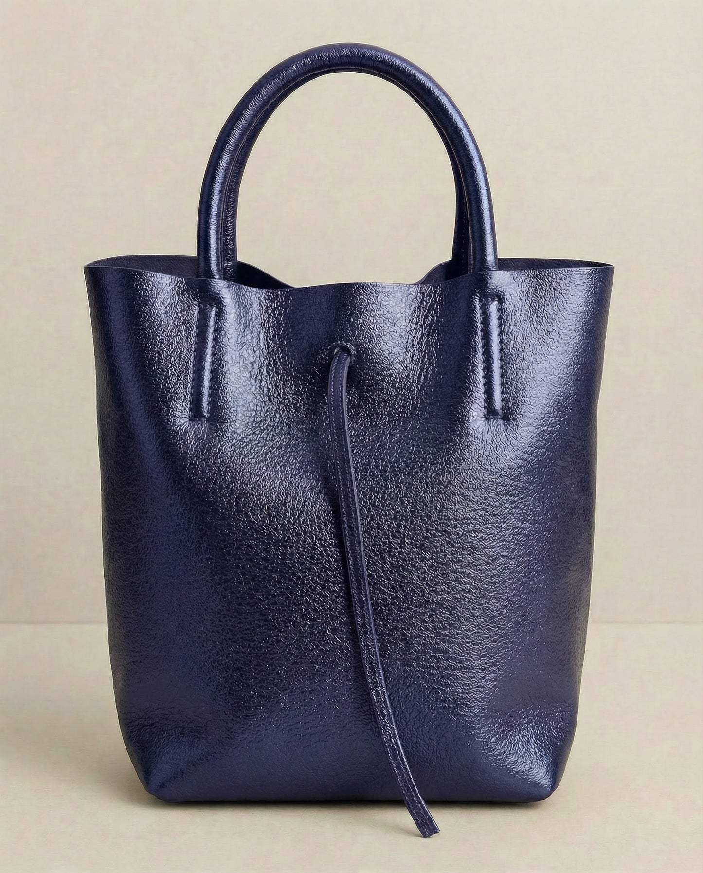 Mini tote in metallic indigo leather with structured silhouette and top handles, sleek and compact design.