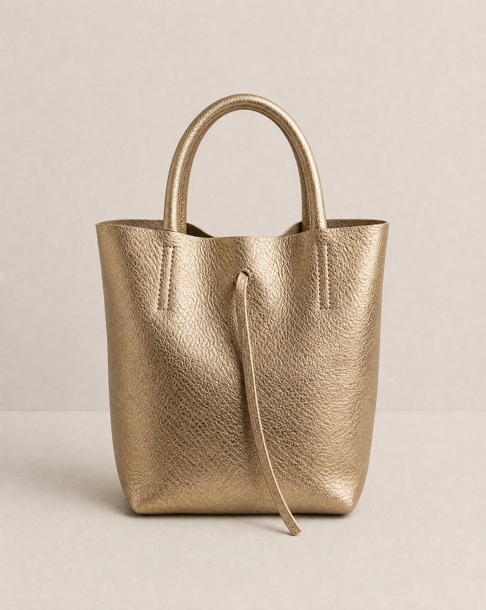Mini tote in metallic Antique gold leather with structured silhouette and top handles, sleek and compact design.