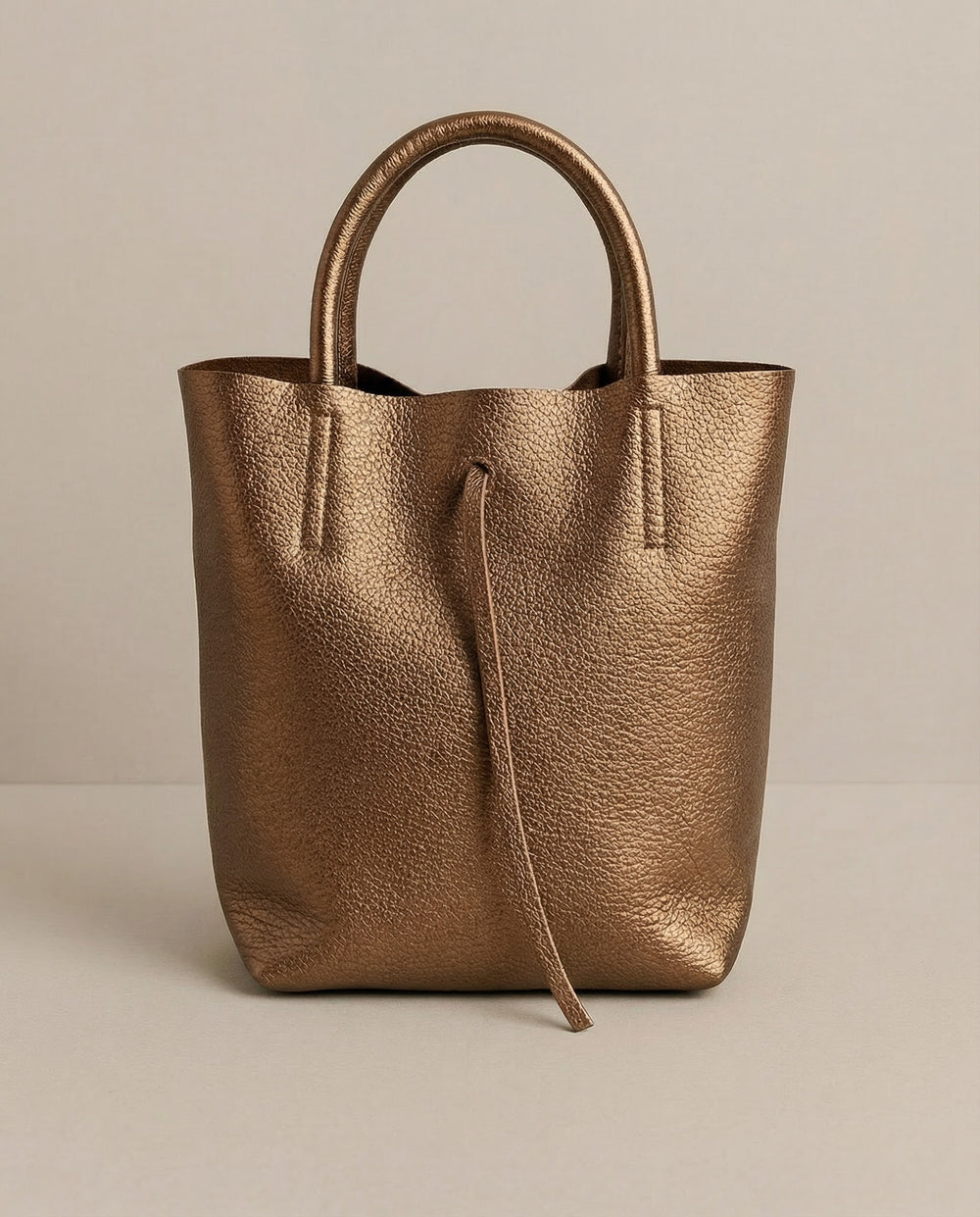 Mini tote in metallic bronze leather with structured silhouette and top handles, sleek and compact design. 