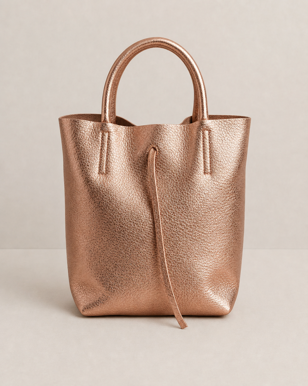 Mini tote in metallic Rose gold leather with structured silhouette and top handles, sleek and compact design. 