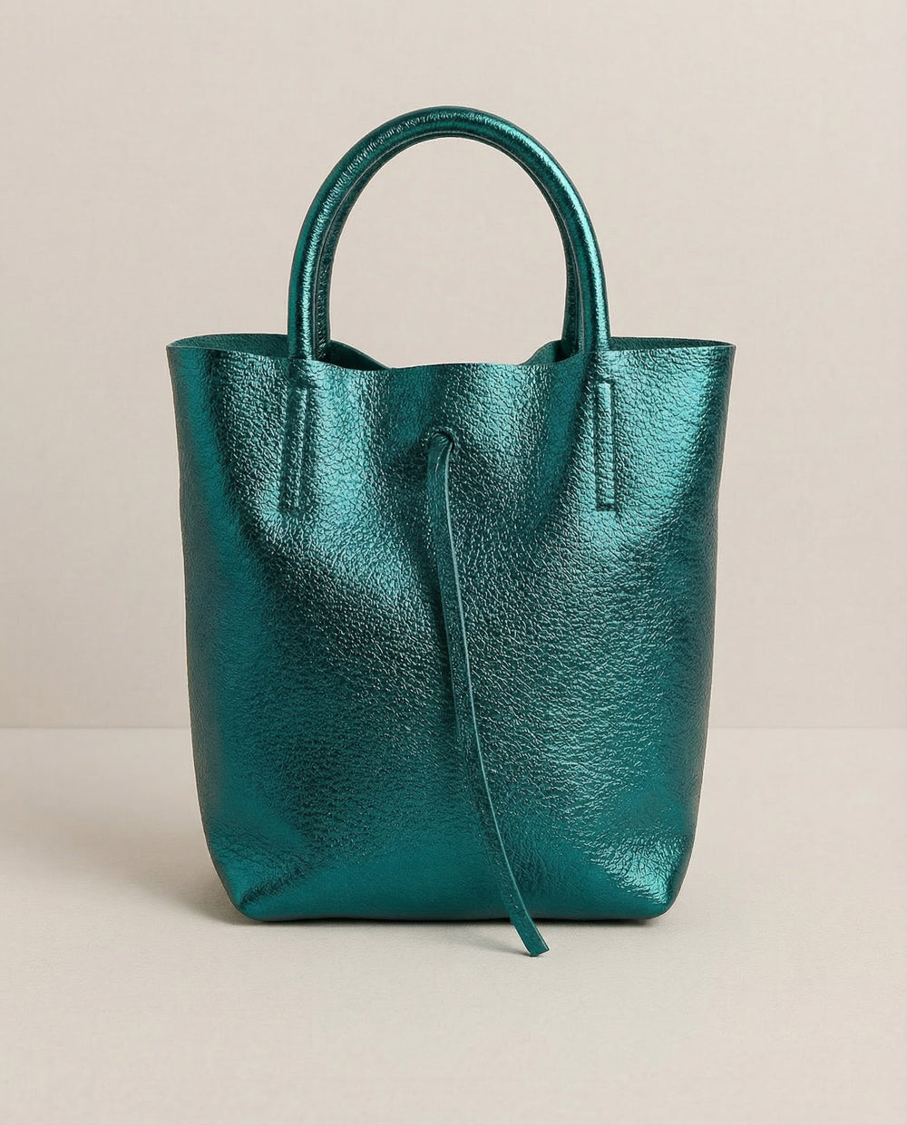 Mini tote in metallic teal leather with structured silhouette and top handles, sleek and compact design.