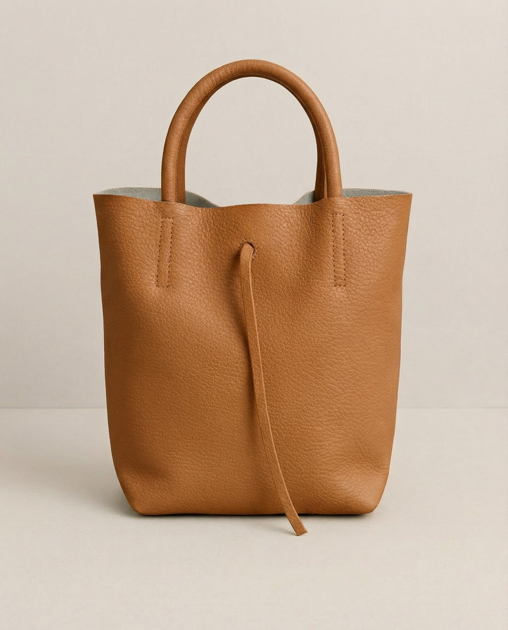 Caramel pebble leather mini tote with structured silhouette, detachable crossbody strap, compact interior, and genuine Italian craftsmanship.