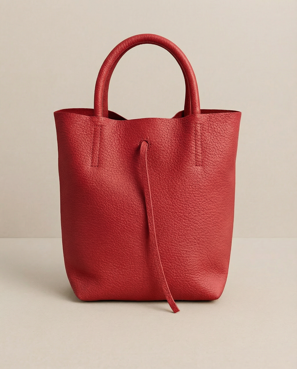 Red pebble leather mini tote with structured silhouette, detachable crossbody strap, compact interior, and genuine Italian craftsmanship.