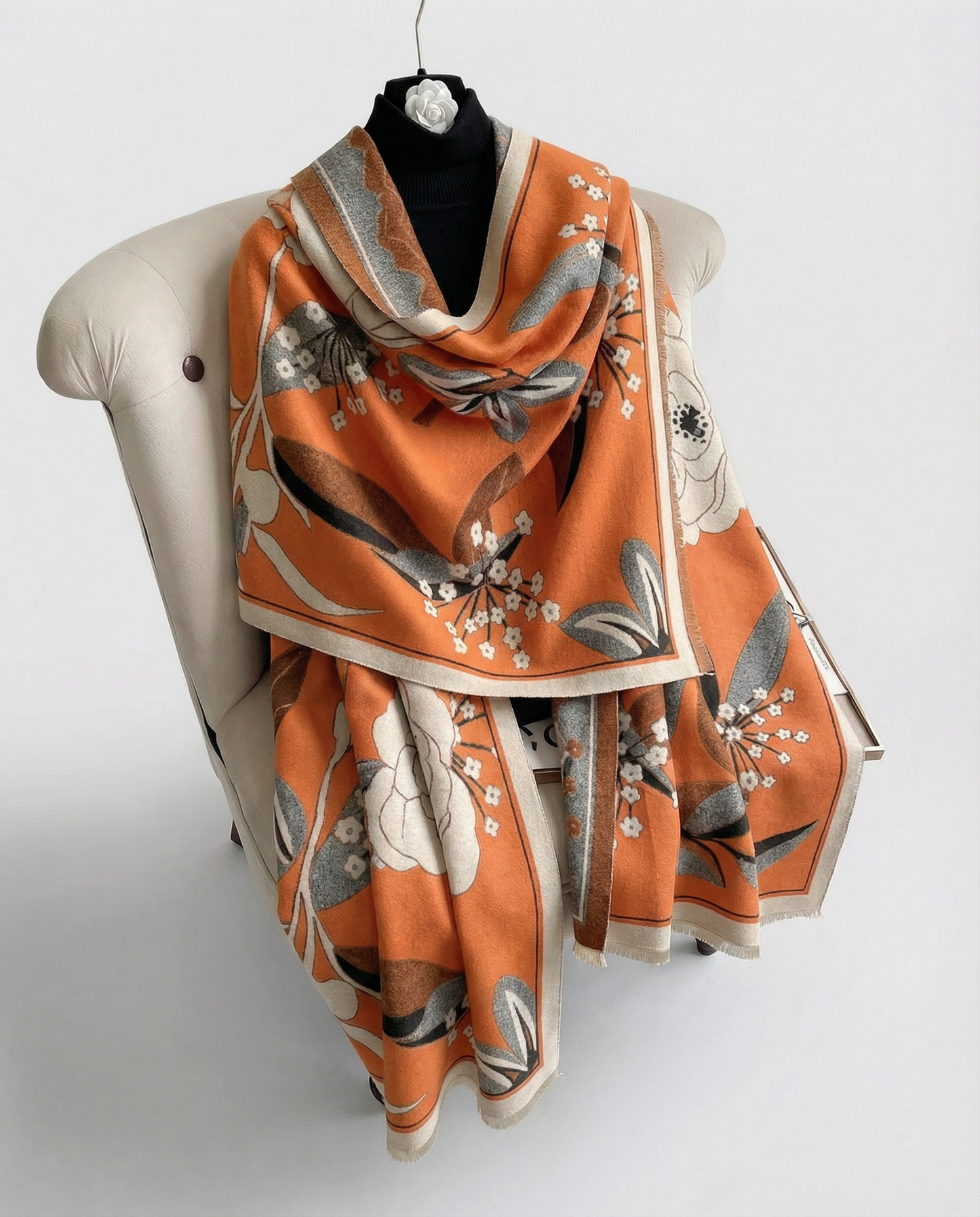 Orange decorative scarf with floral pattern draped over a chair on a white background