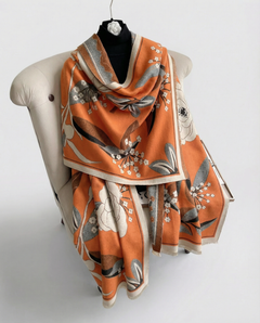 Orange decorative scarf with floral pattern draped over a chair on a white background, view 2