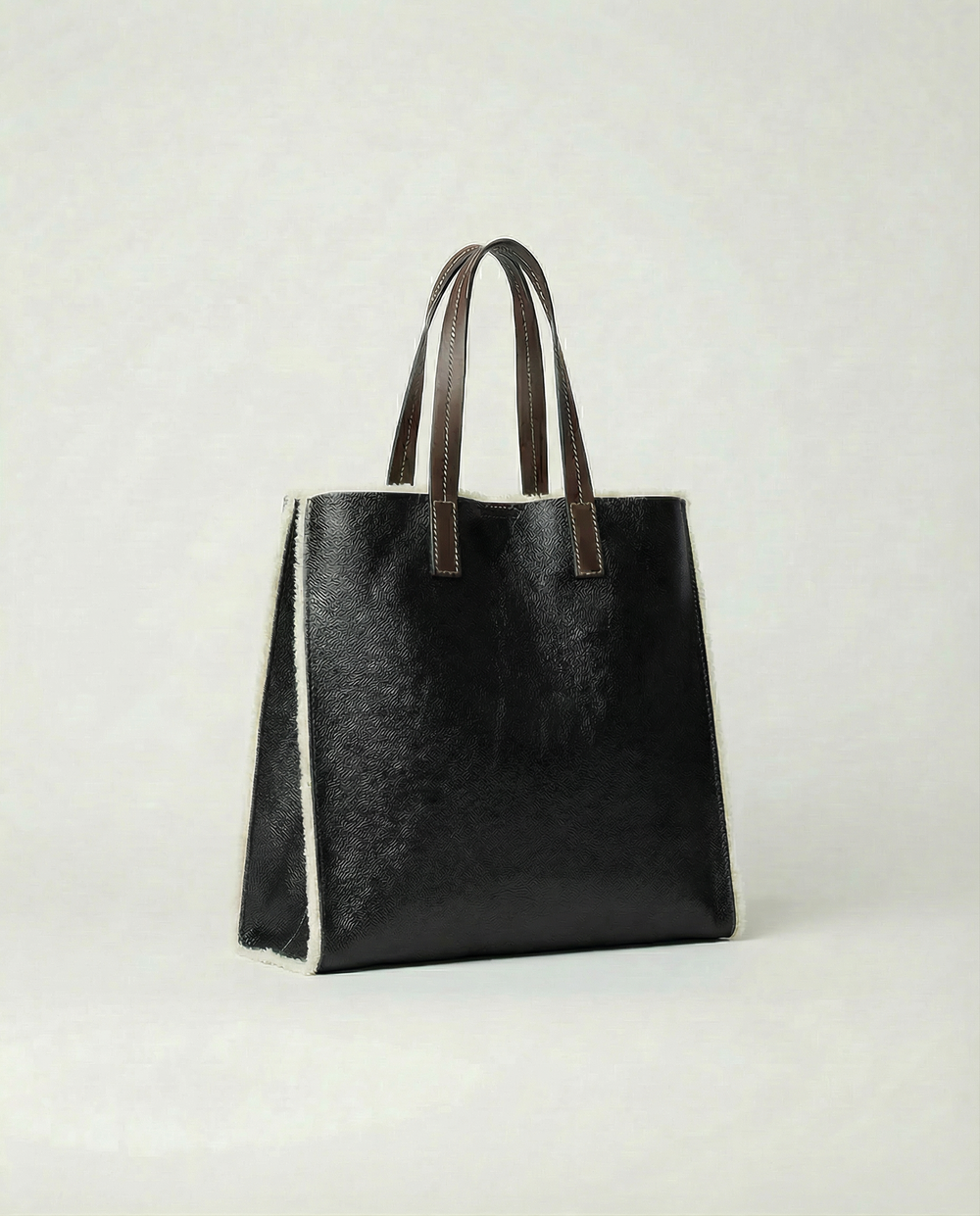 Black leather tote bag with brown handles on a light gray background