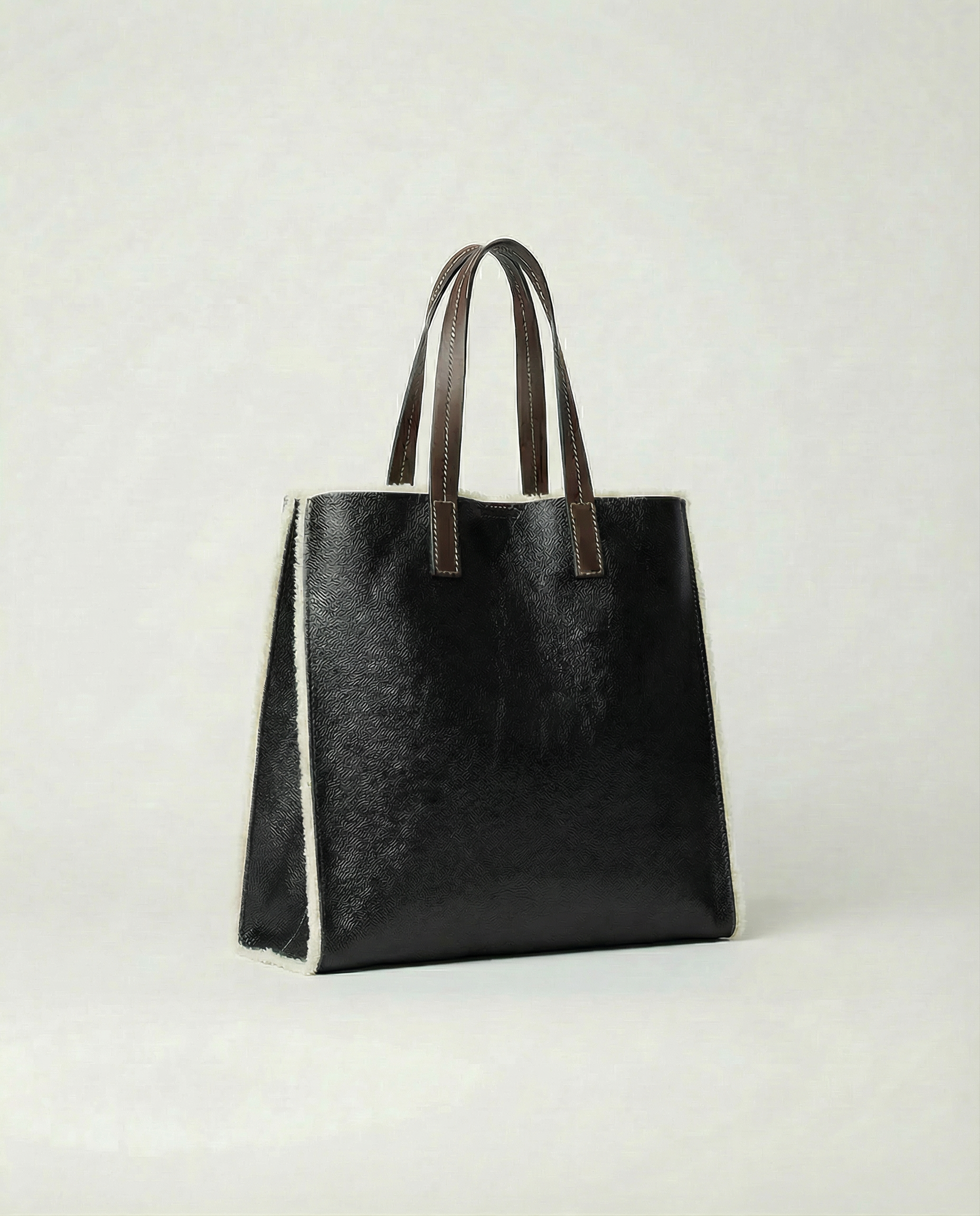 Black leather tote bag with brown handles on a light gray background