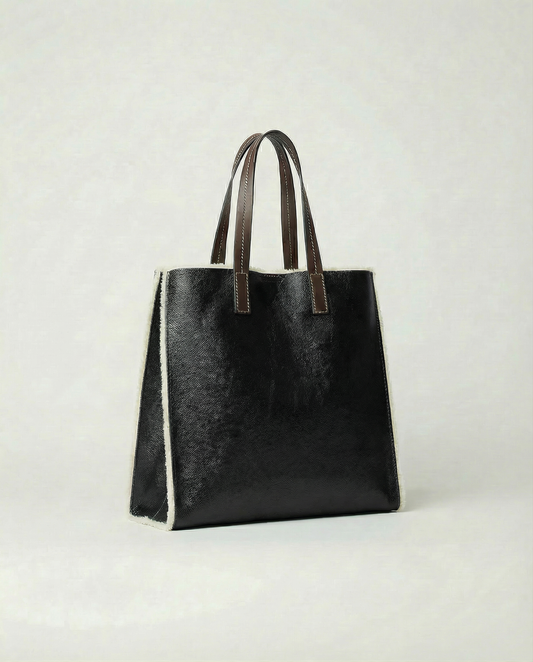 Black leather tote bag with brown handles on a light gray background