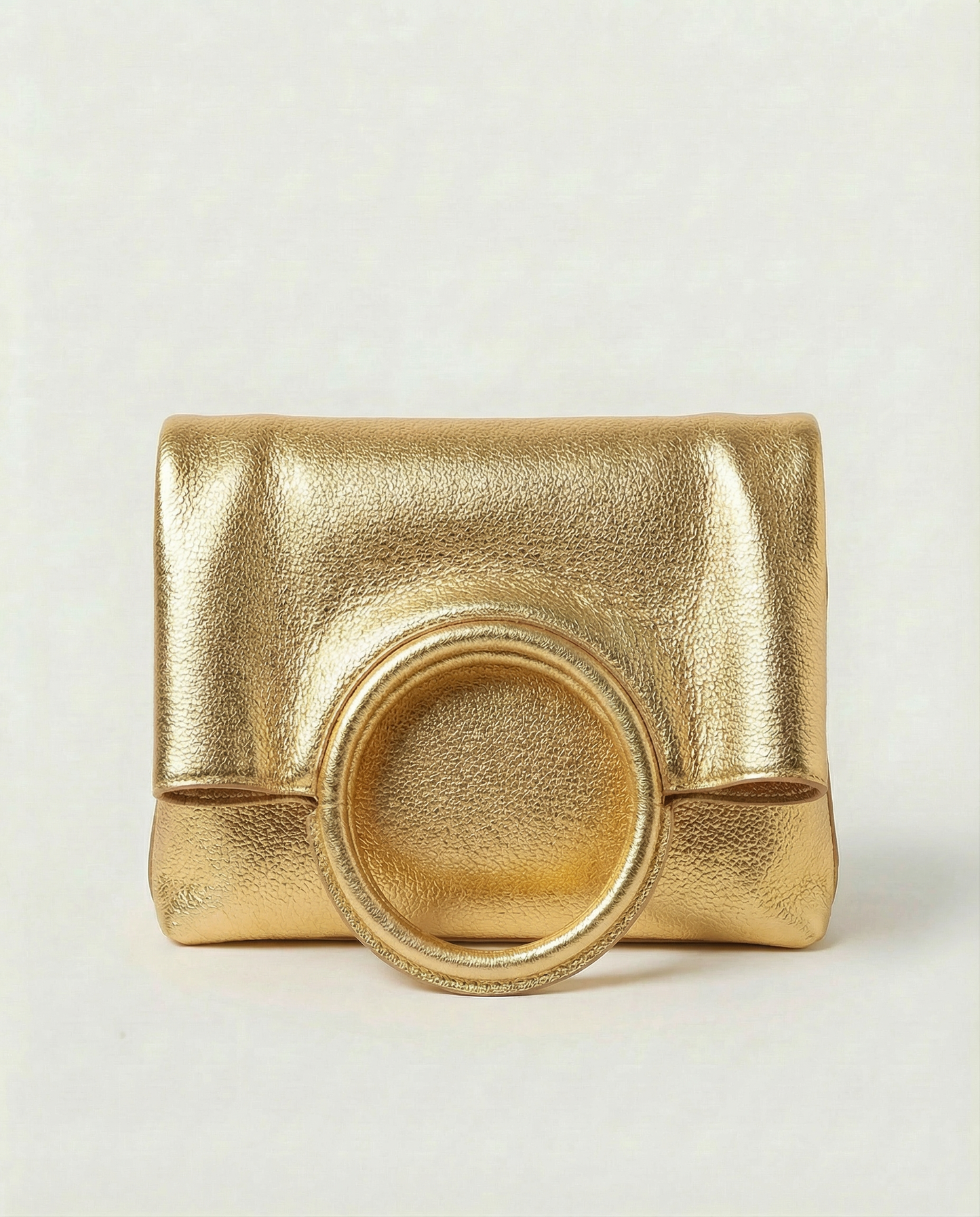 Gold metallic ring bag with circular handles on a light gray background