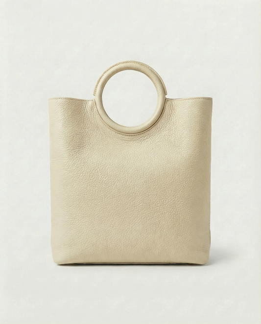 Ring Bag in pebble leather ivory with circular ring handle and structured silhouette.