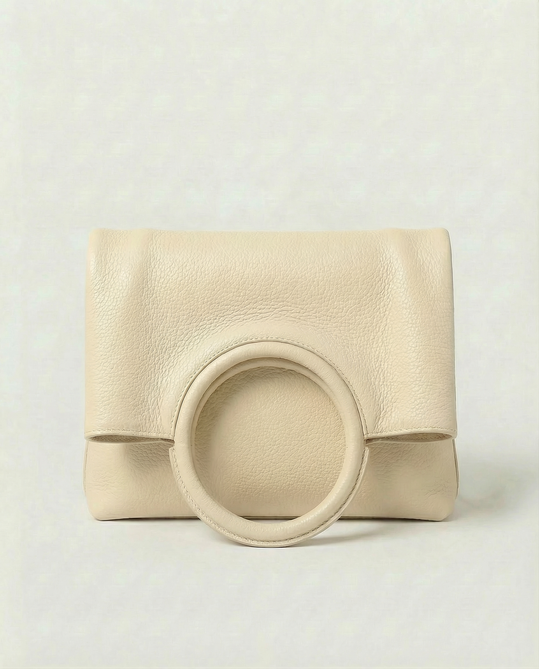 Ring Bag in pebble leather ivory with circular ring handle and structured silhouette.